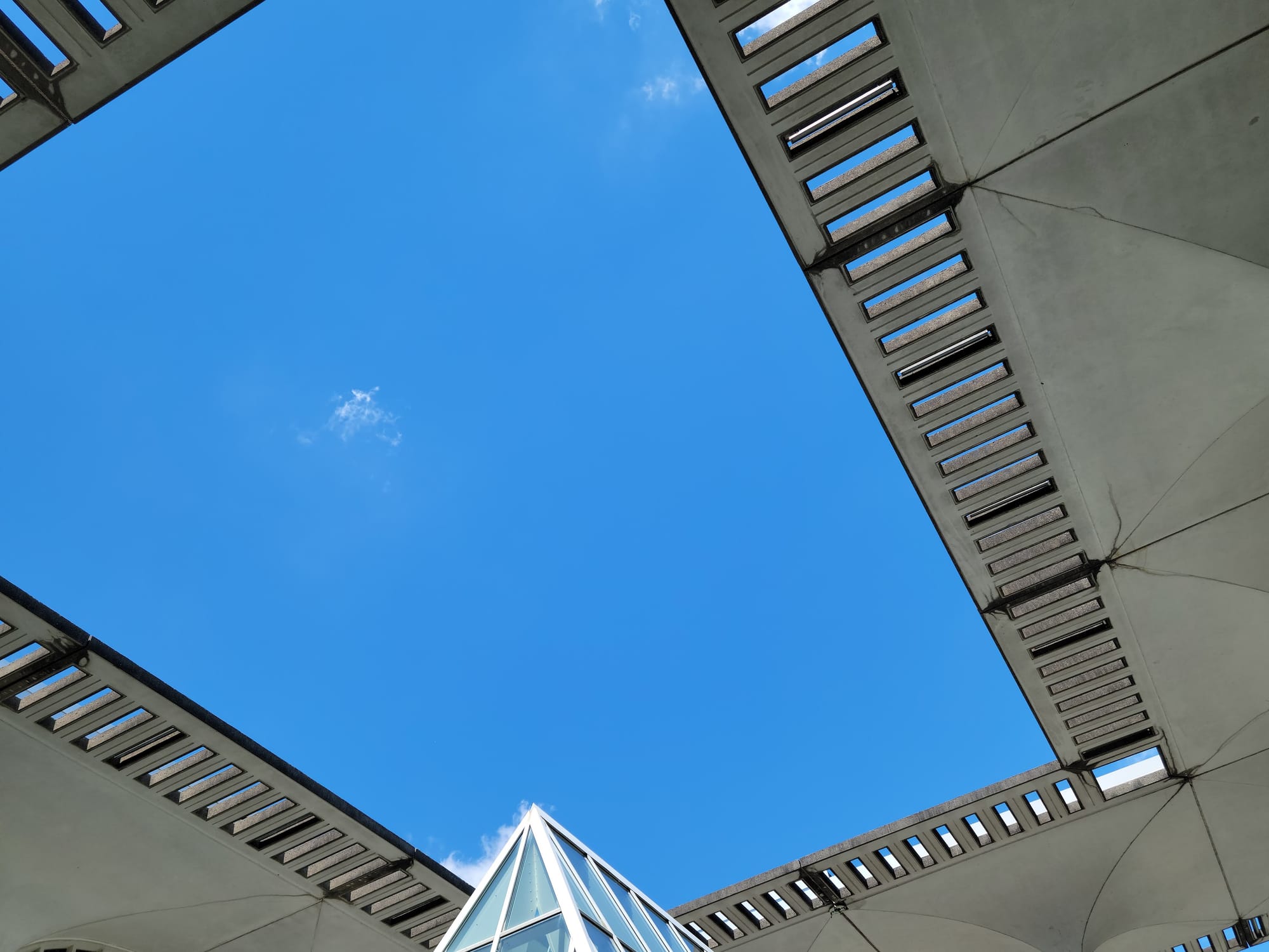 A photo of a cut-out in a concrete canopy on the University at Albany campus revealing a bright blue sky with few clouds