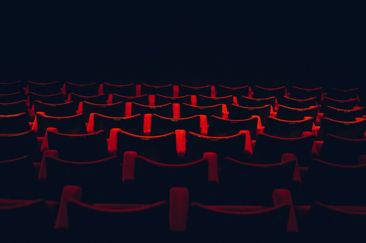 A photograph of red velvet theater seating descending in rows into shadowed darkness.