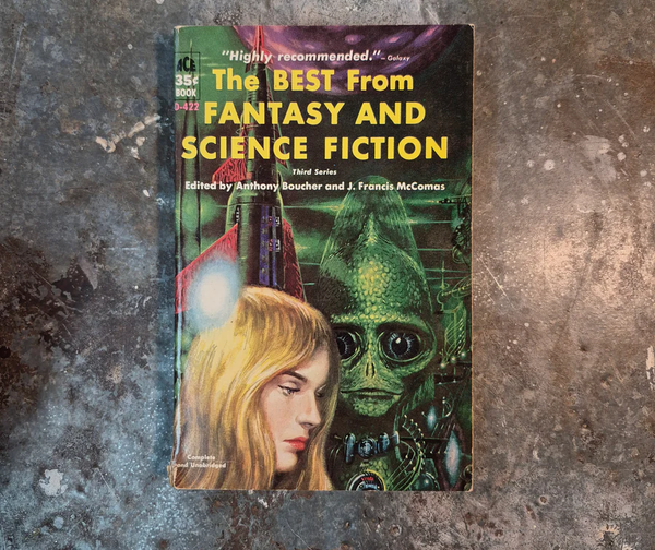 A vintage paperback book titled the The Best From Fantasy and Science Fiction with a beautiful blond woman and a green lizard alien standing in front of a rocket ship.