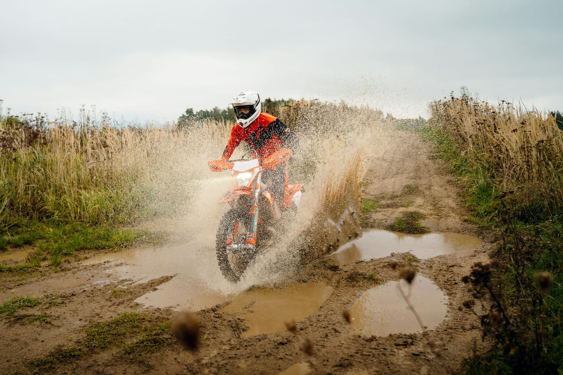 Enduro rider crossing a muddy section of natural off-road terrain.