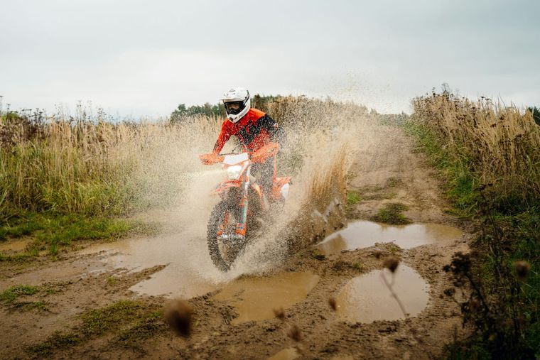 Enduro rider crossing a muddy section of natural off-road terrain.