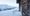 Weathered wooden door of an alpine hut in fresh snow, an old key on a nail with a red Swiss-cross tag, snowy peaks behind.