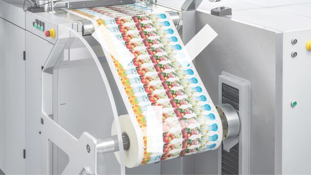 A printed web with a repeating fruit and vegetable design running over the rollers of a digital press.