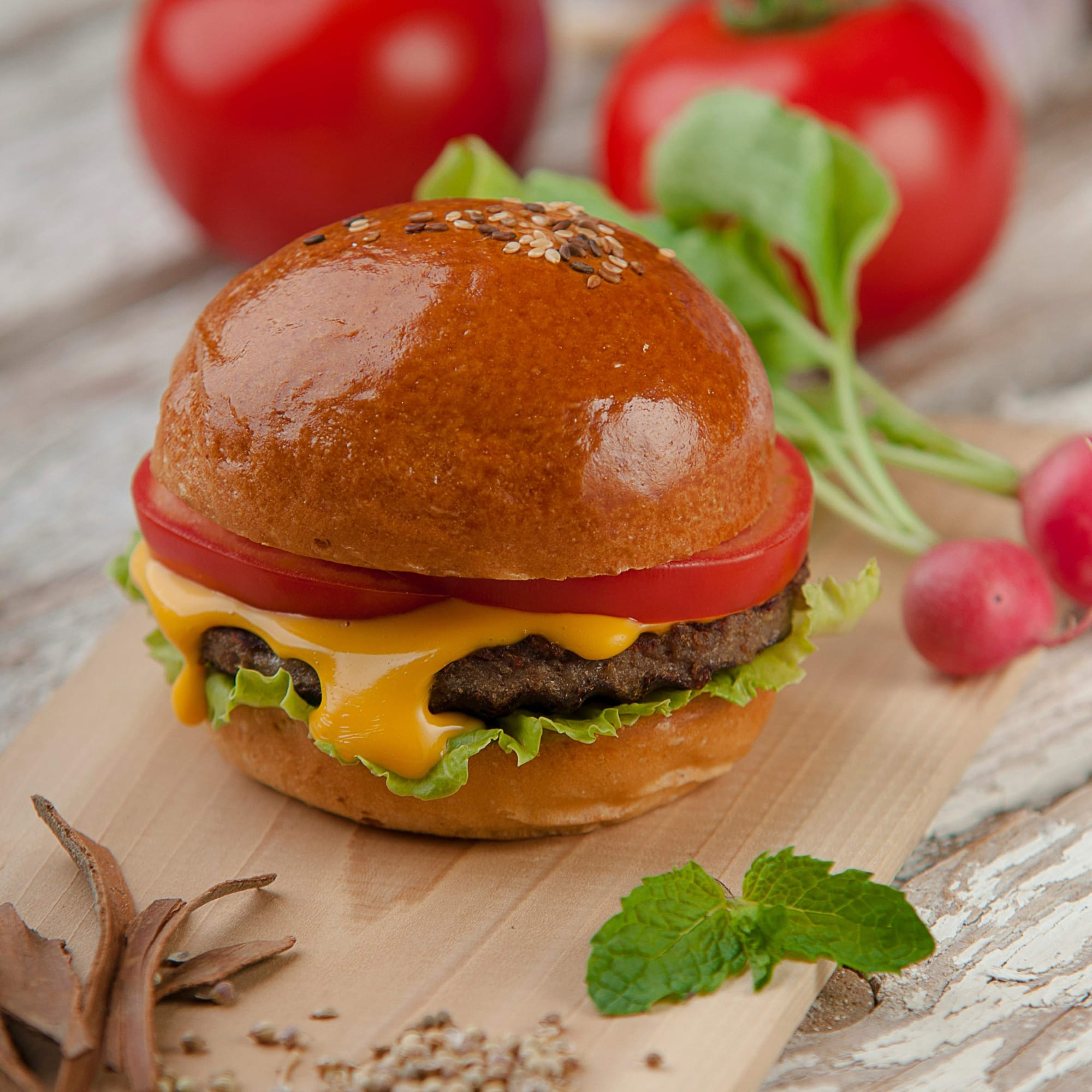 A burger topped with sliced tomato and melted cheese, close up
