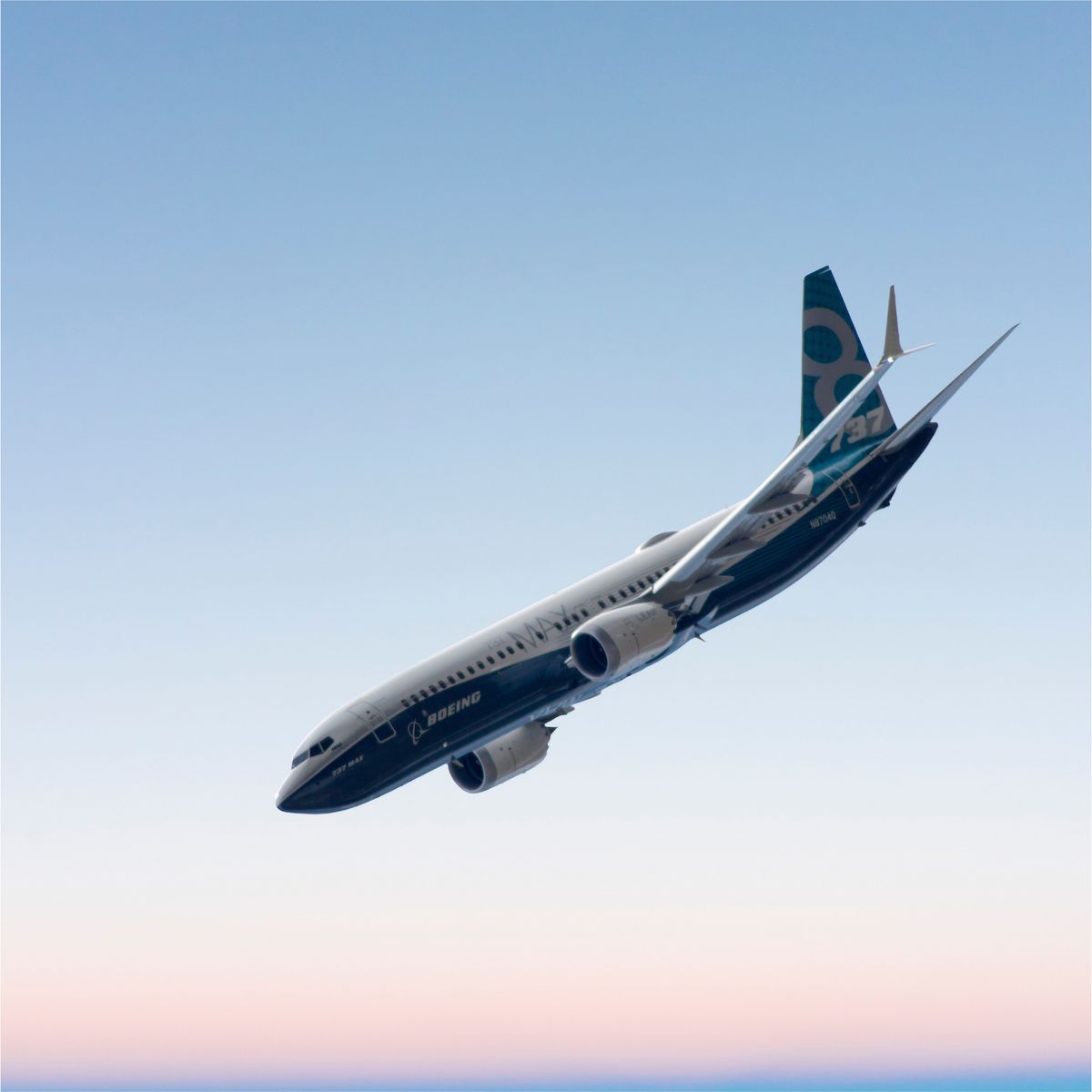 Boeing 737 MAX aircraft flying against a clear blue and pink gradient sky