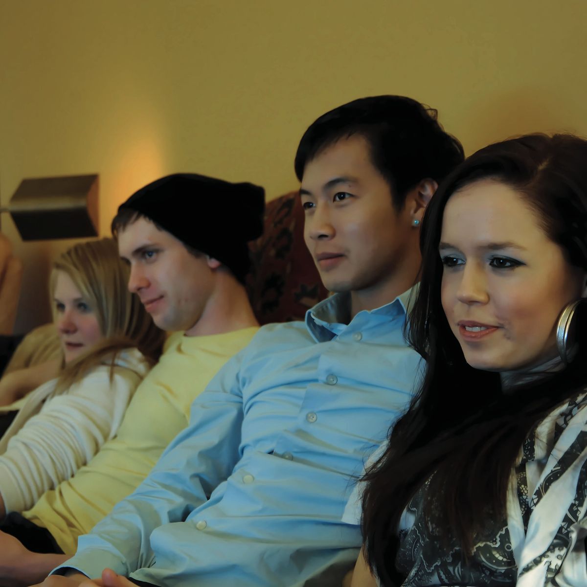 Four roommates sitting on a couch watching television together in a cozy setting