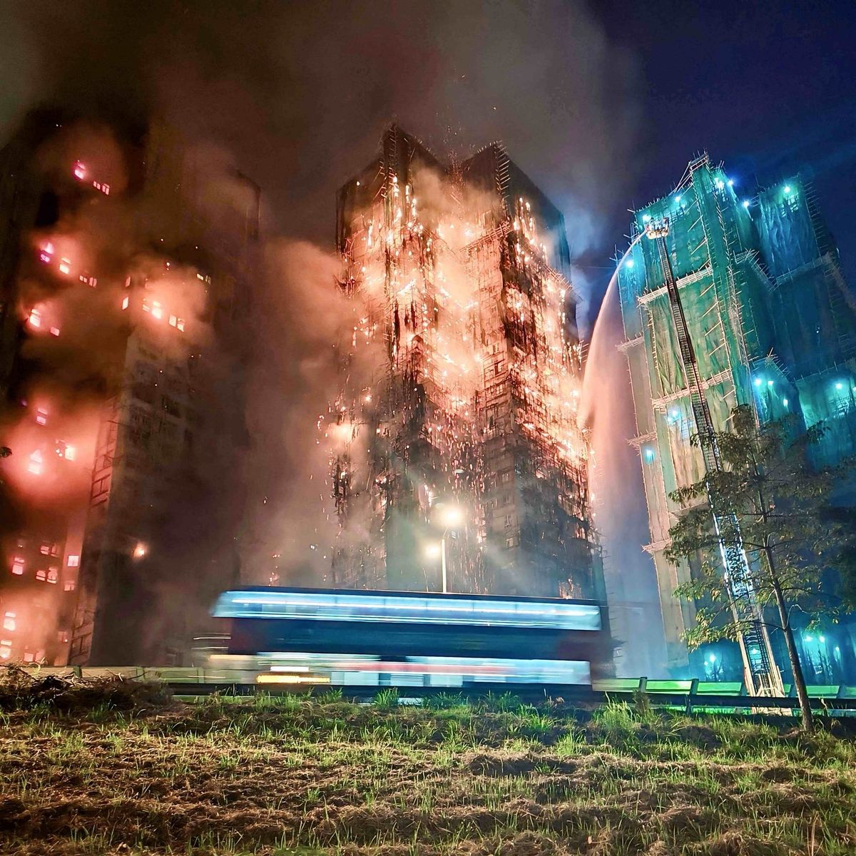 High-rise building engulfed in flames at night with firefighters spraying water