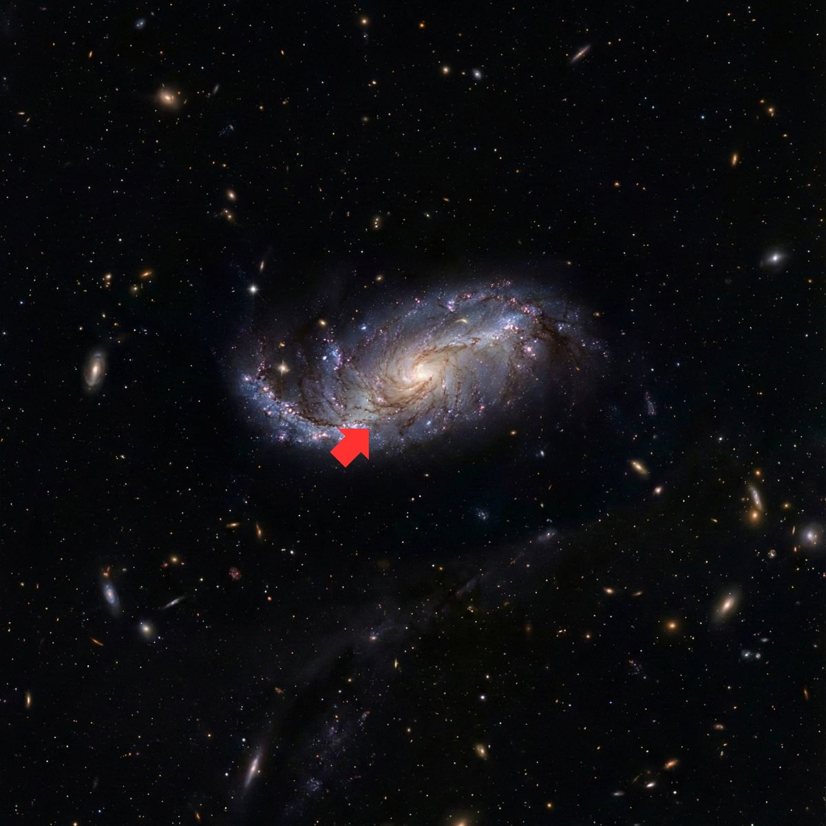 Spiral galaxy in deep space with red arrow pointing to small region