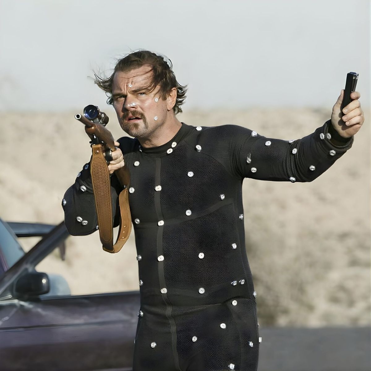 Leonardo DiCaprio in motion capture suit holding rifle in desert