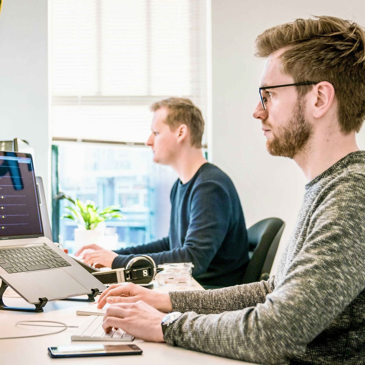 Two men in sweaters working at laptops in bright office