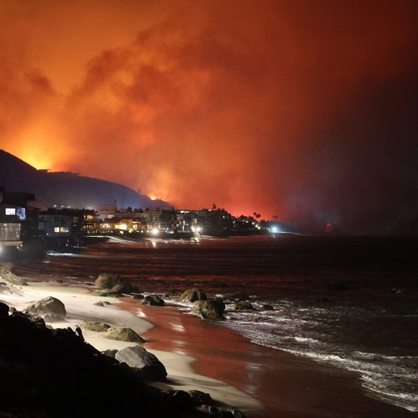 A wildfire glows orange over coastal homes and hills near Los Angeles at night