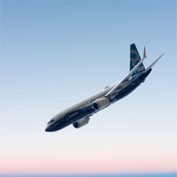 Boeing 737 MAX aircraft flying against a clear blue and pink gradient sky