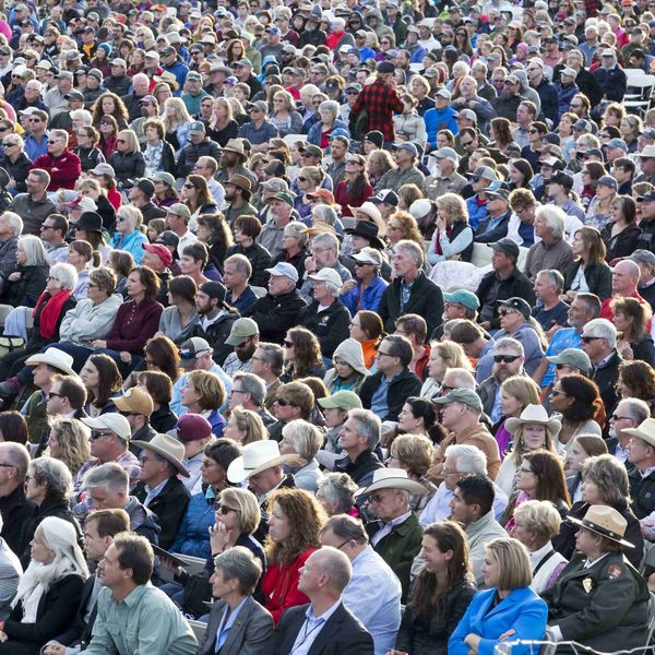 Large crowd of people seated outdoors, many wearing hats and jackets