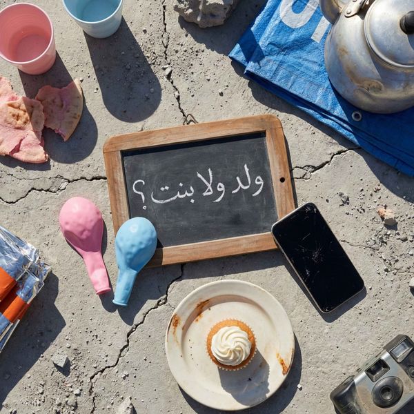 Gender reveal party items arranged on cracked concrete with Arabic chalkboard sign