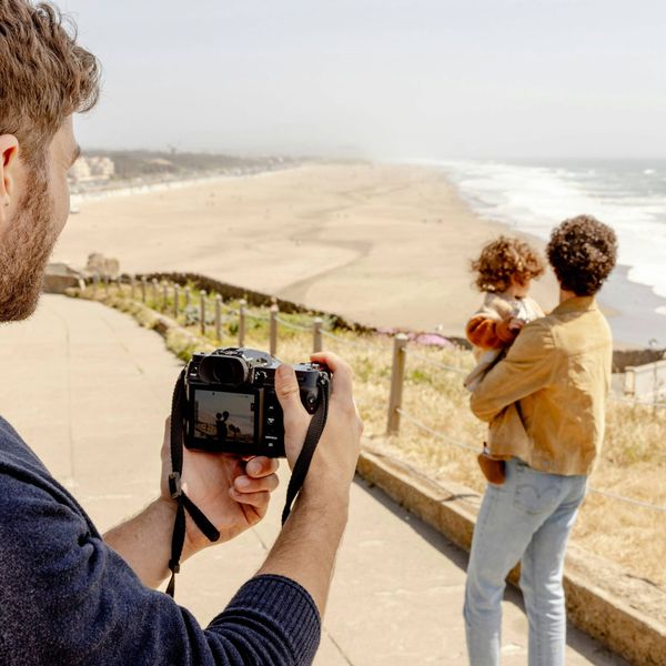 Man holds camera, photographing adult holding child near the ocean
