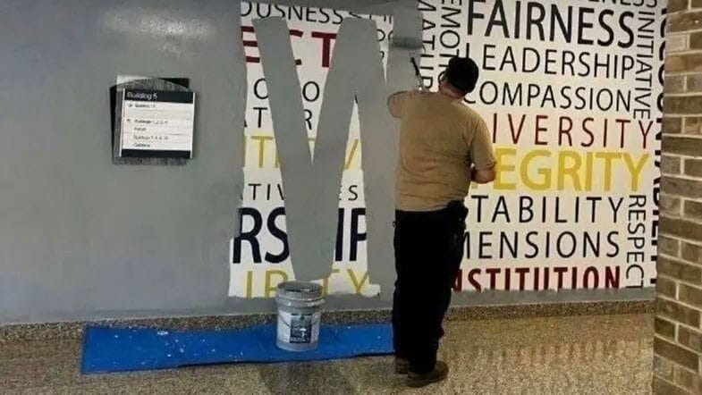 A man paints over a mural of words extolling human virtues.