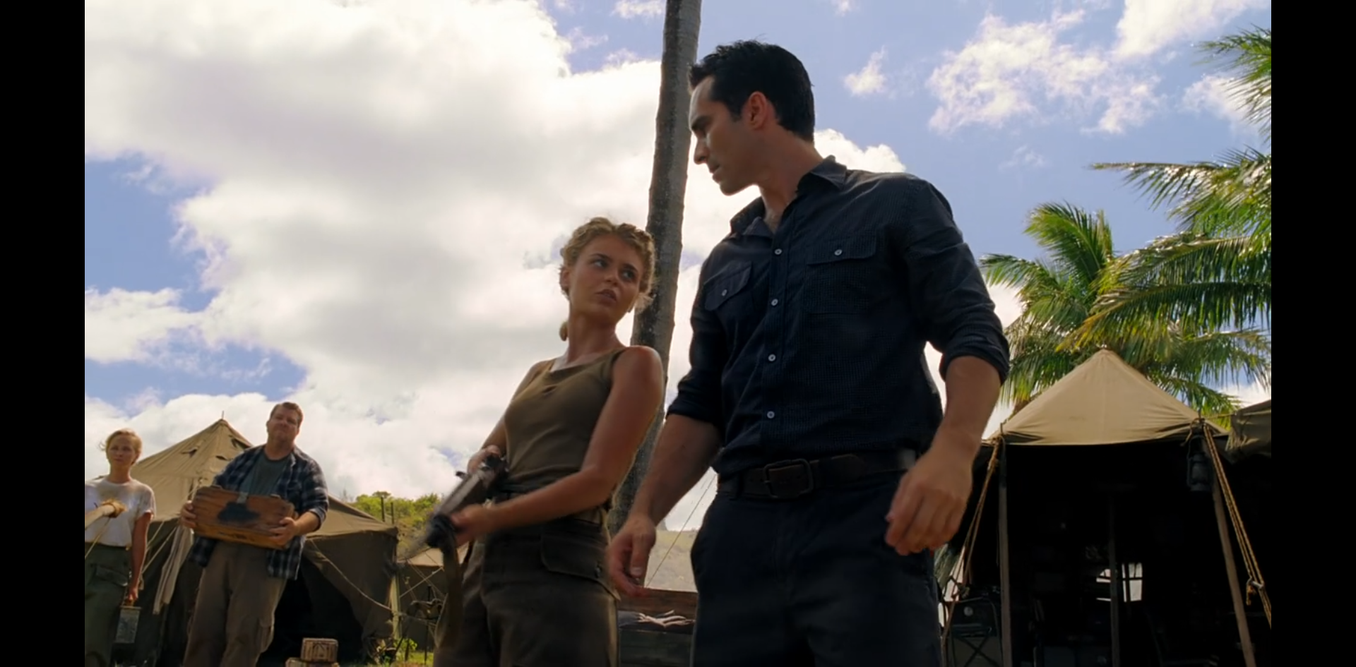 Ellie and Alpert in the foreground in front of military tents. Some diffident-looking extras in background.