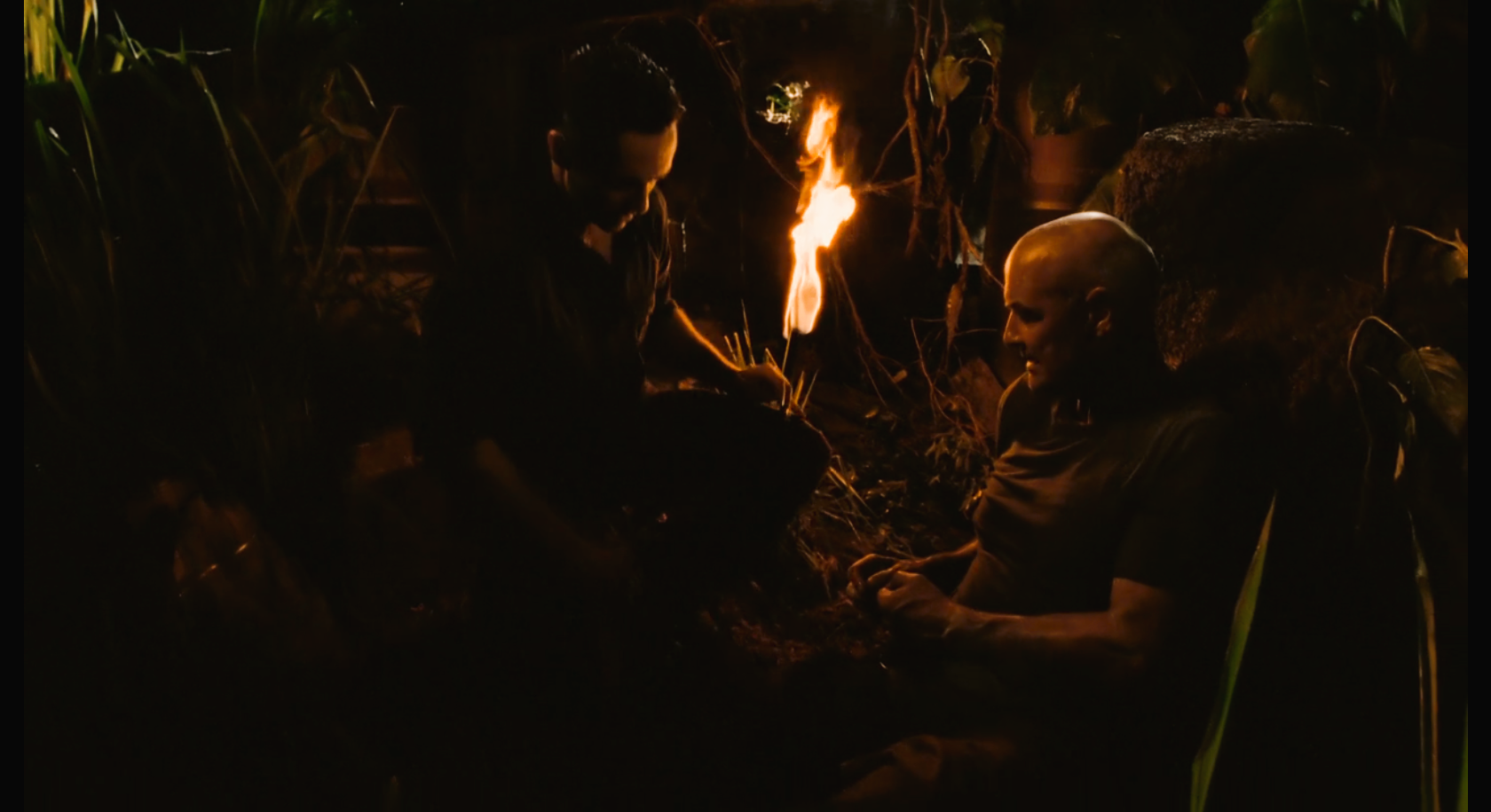 Richard Alpert tends to John Locke's wounded leg by the light of a torch.