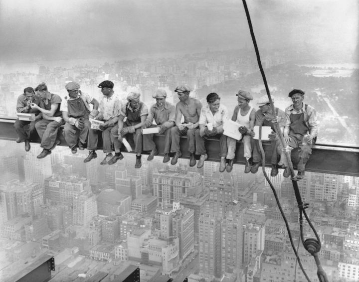 Construction workers having lunch sitting on a girder of the skyscraper they're building.