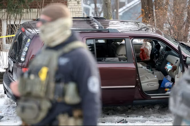 An ICE agent stands in front of Renee Good's minivan. The door is open, showing a bloody driver's side airbag.