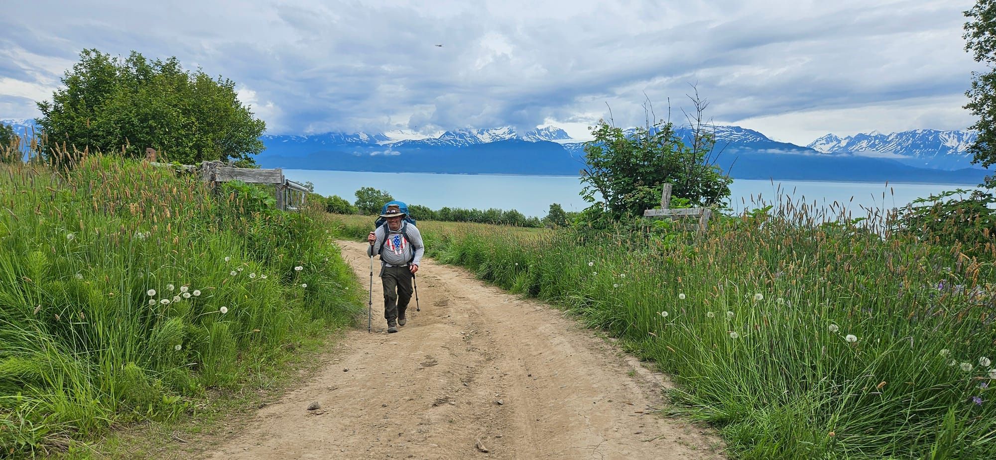 Two people walk a trail toward Kachemak Bay and the Alaska mountains.