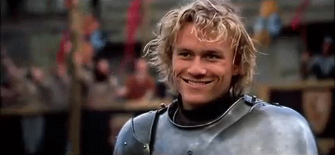 heath ledger in metal armor winking at someone off camera with a crowd of cheering people behind him, from "a knight's tale"