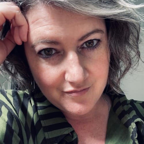 meg as androgynous person with grey hair and a green and black striped shirt