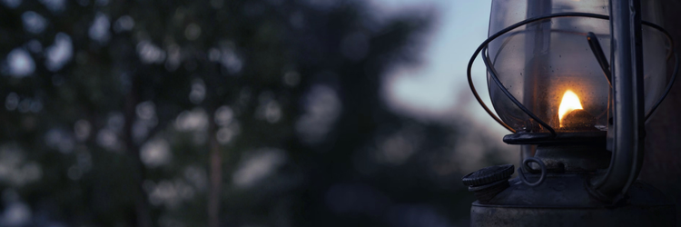 close up photograph of oil lantern, lit and glowing, with trees and sky in the backgr