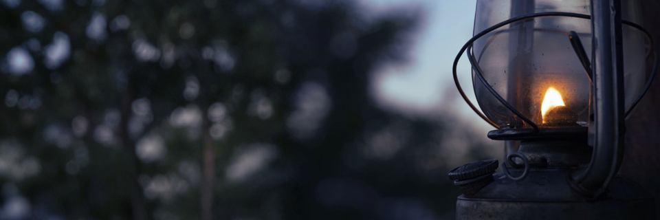 close up photograph of oil lantern, lit and glowing, with trees and sky in the backgr