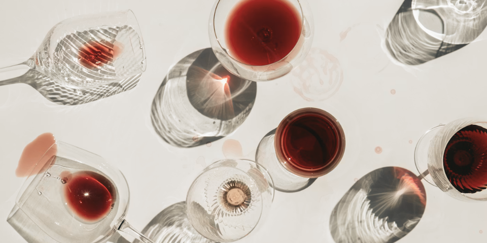 wine glasses filled with red wine on a white background, some spilled and some upright