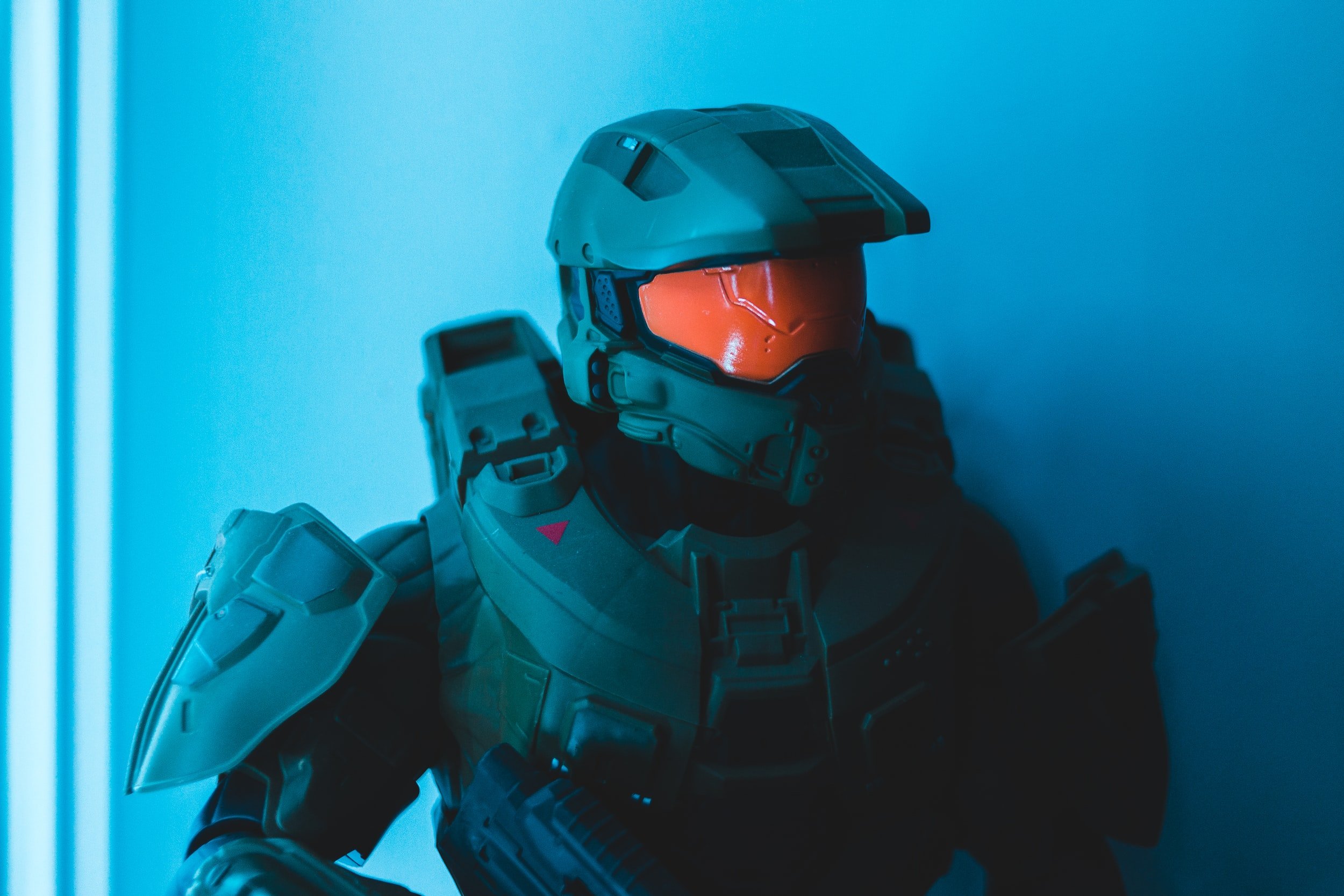 A Halo Spartan warrior head and torso shot at an angle against a medium blue wall found in a sterile environment such as a lab or hospital.