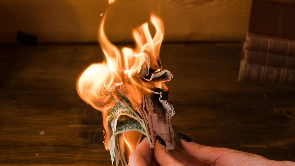 A hand holds a bundle of money, which is burning
