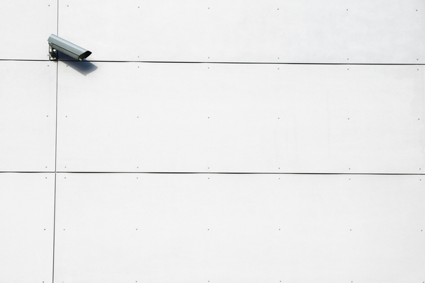 A surveillance camera on a wall looks to the side