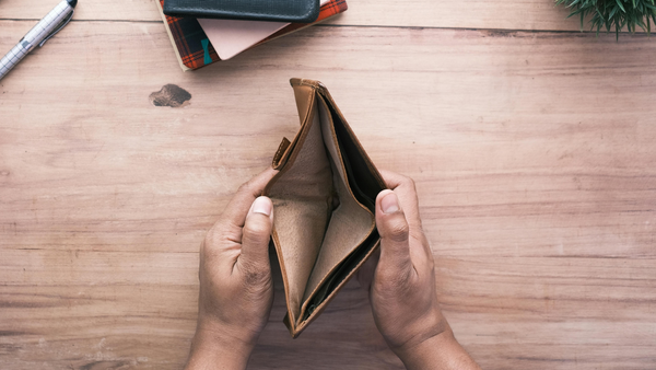 A pair of hands hold open an empty wallet on a wooden desk