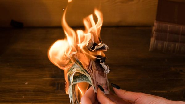 A hand holds a bundle of money, which is burning