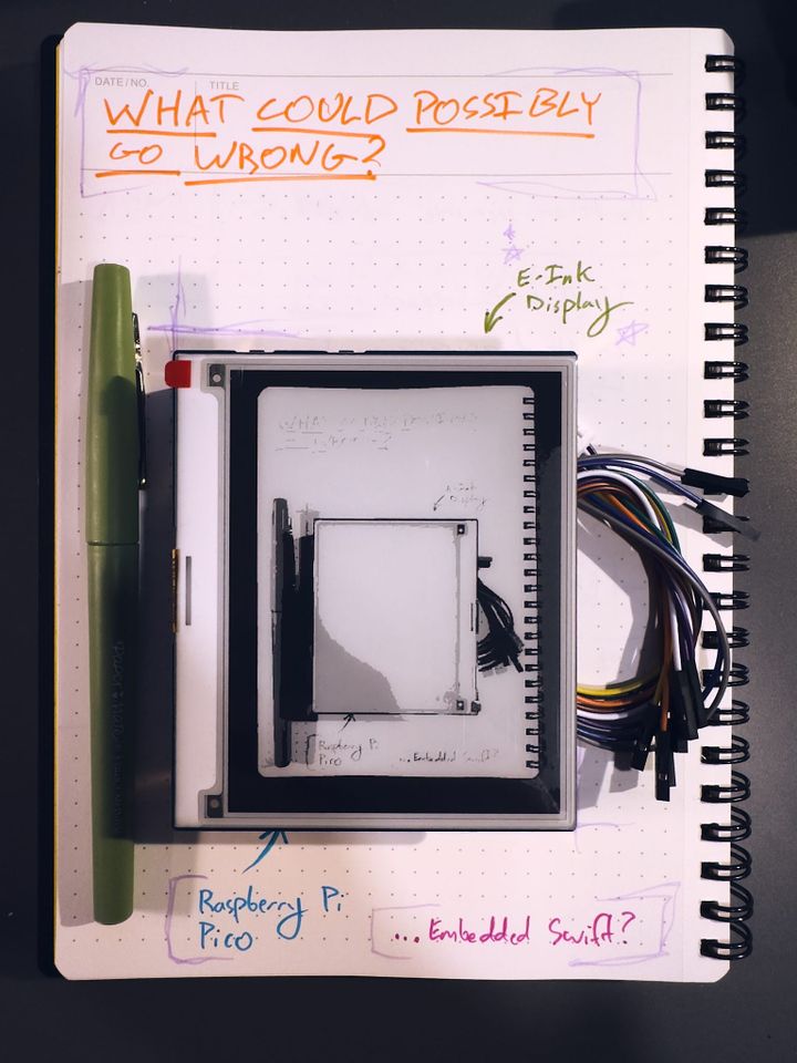 A photograph of a grayscale e-ink display placed on top of a notebook with various captions and callouts