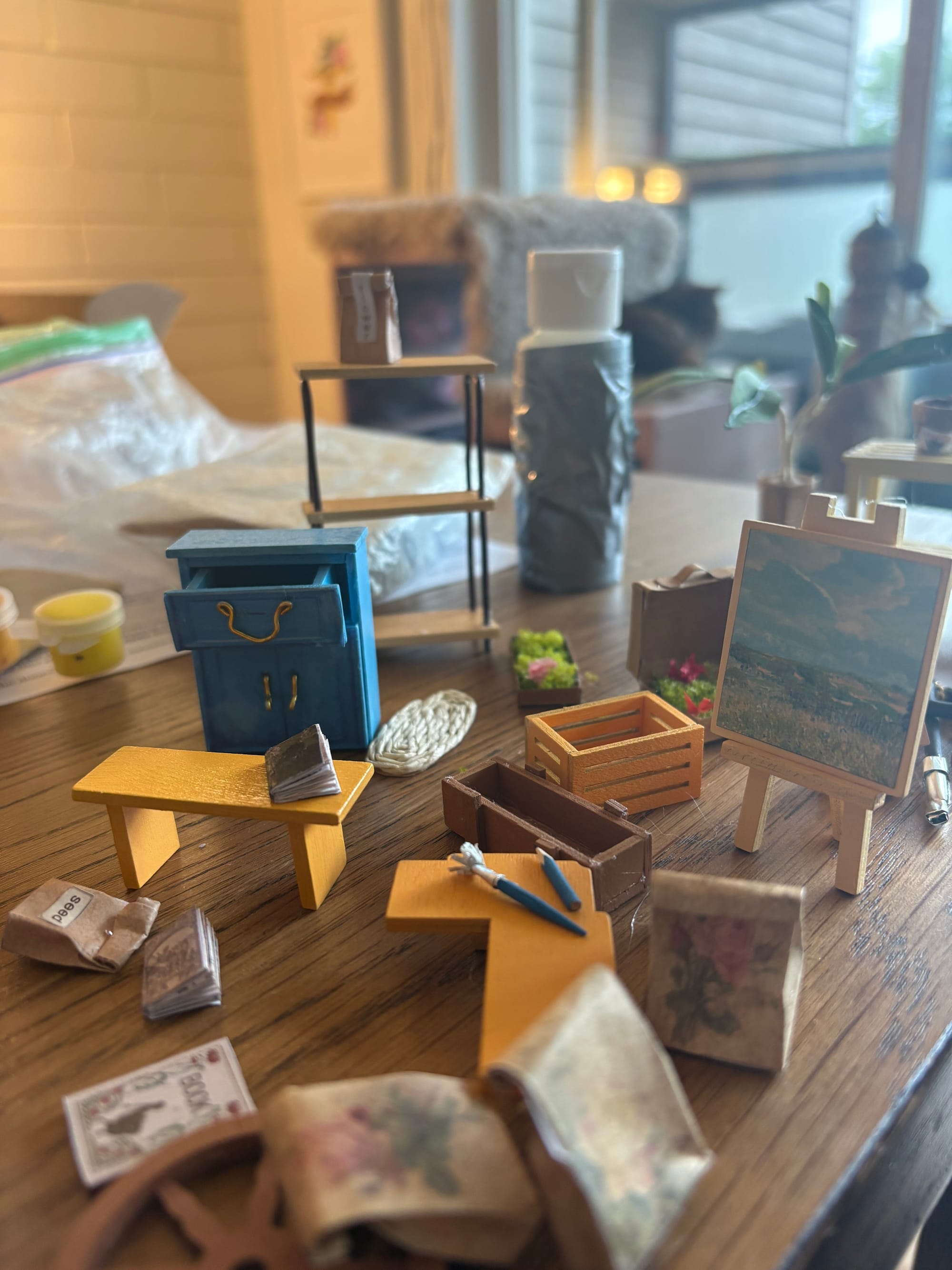A close-up of several miniatures including paper bags, shelves, books, an easel and paint brush, and plants.