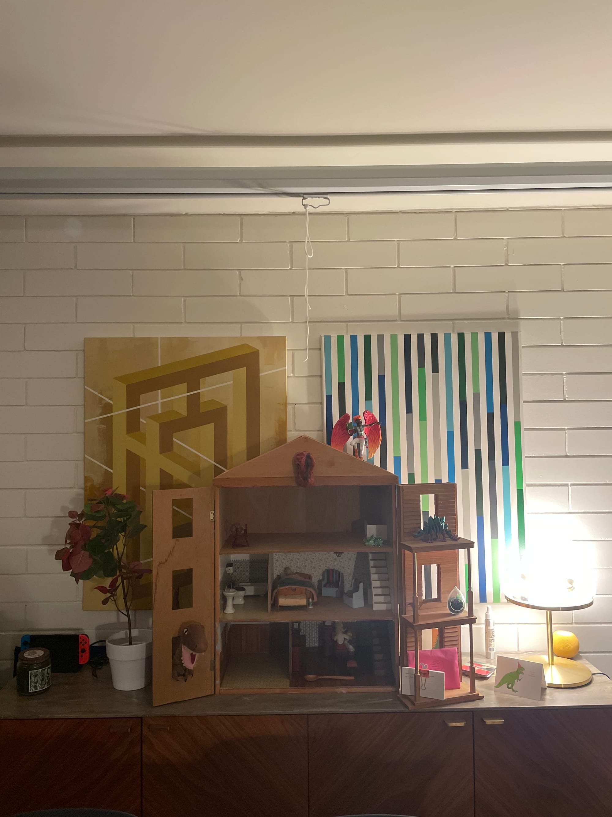 A three-story dollhouse sits on a sideboard with its fold-away front opened to display a mostly empty and unfinished interior.