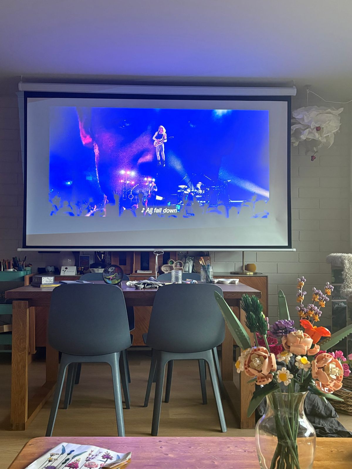 A projector screen shows the open credits of The Vampire Lestat. In the background, a dollhouse and some craft supplies. In the foreground, a recently completed Lego bouquet.