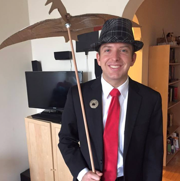 Kyle in black suit with felt hat, red tie, and over-the-should pterodactyl