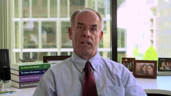 Man in front of window, books, and family photo speaks to camera