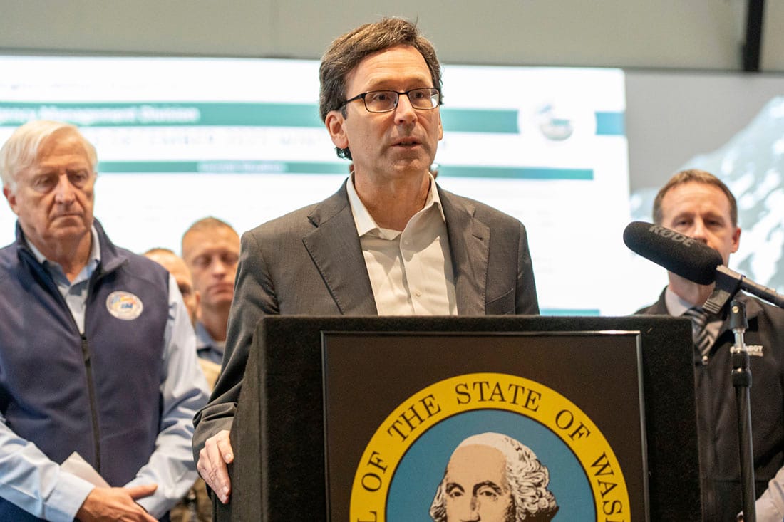 Bob Ferguson and state officials stand behind a podium with the seal of the state of Washington on it