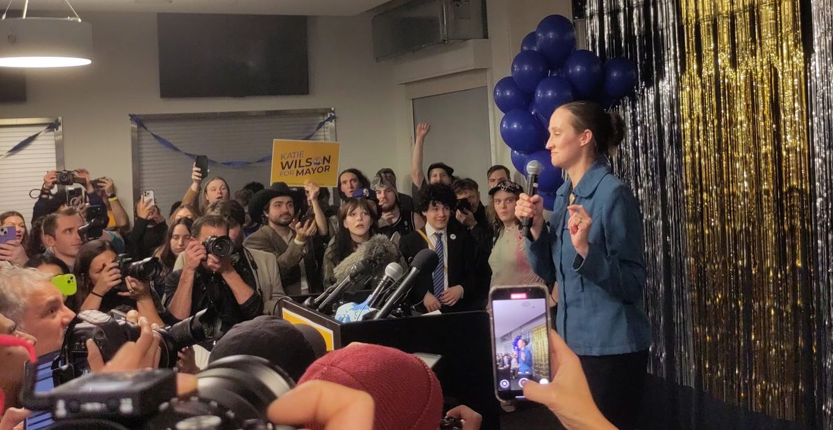 Katie Wilson faces a crowd of supporters and photographers with a microphone in her hand.
