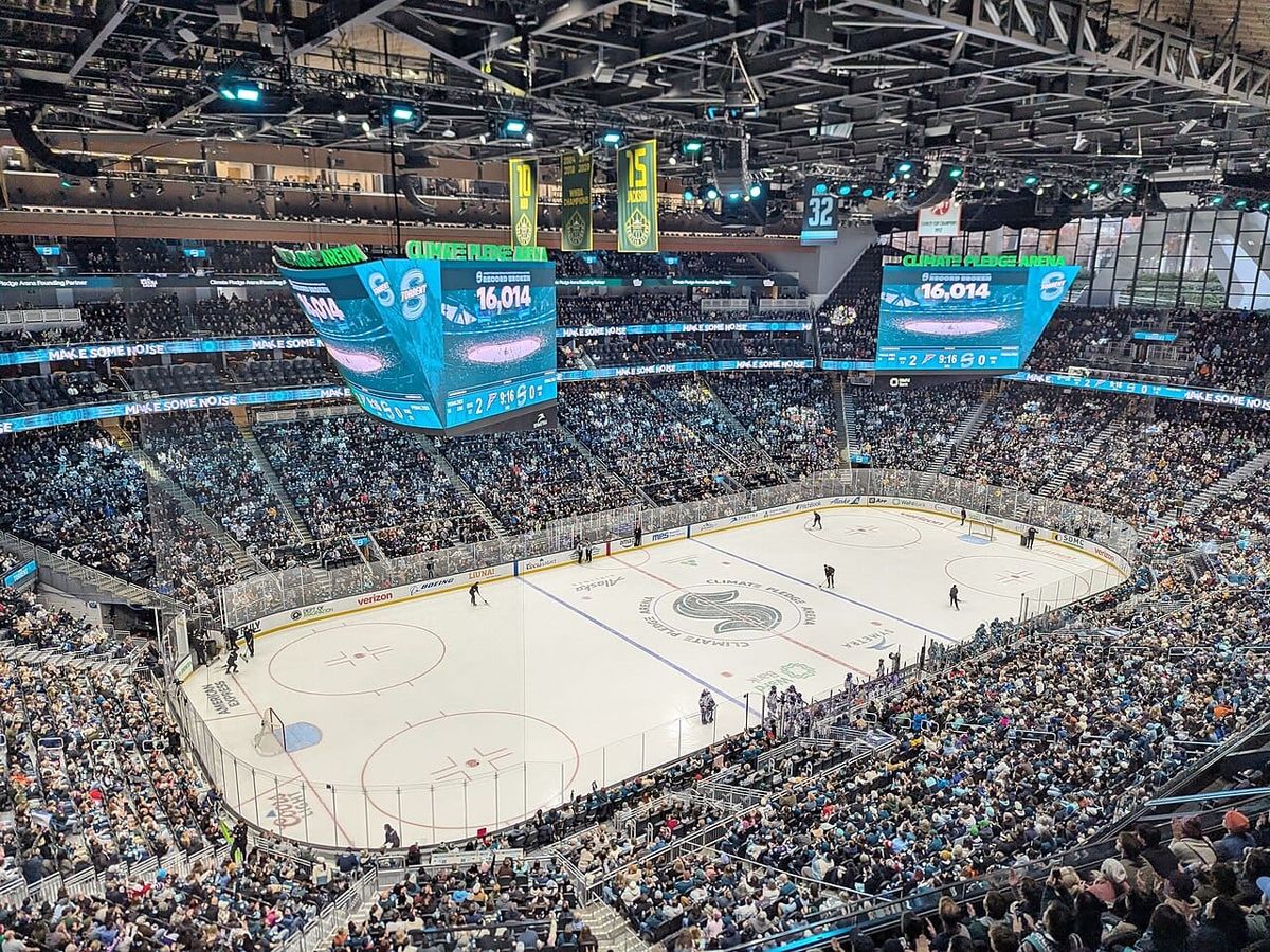 A crowd of fans watch a hockey game in a large stadium
