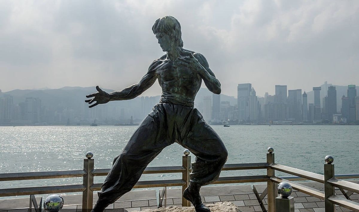 A sculpture of a man doing martial arts in front of a hazy skyline of skyscrapers on a bay