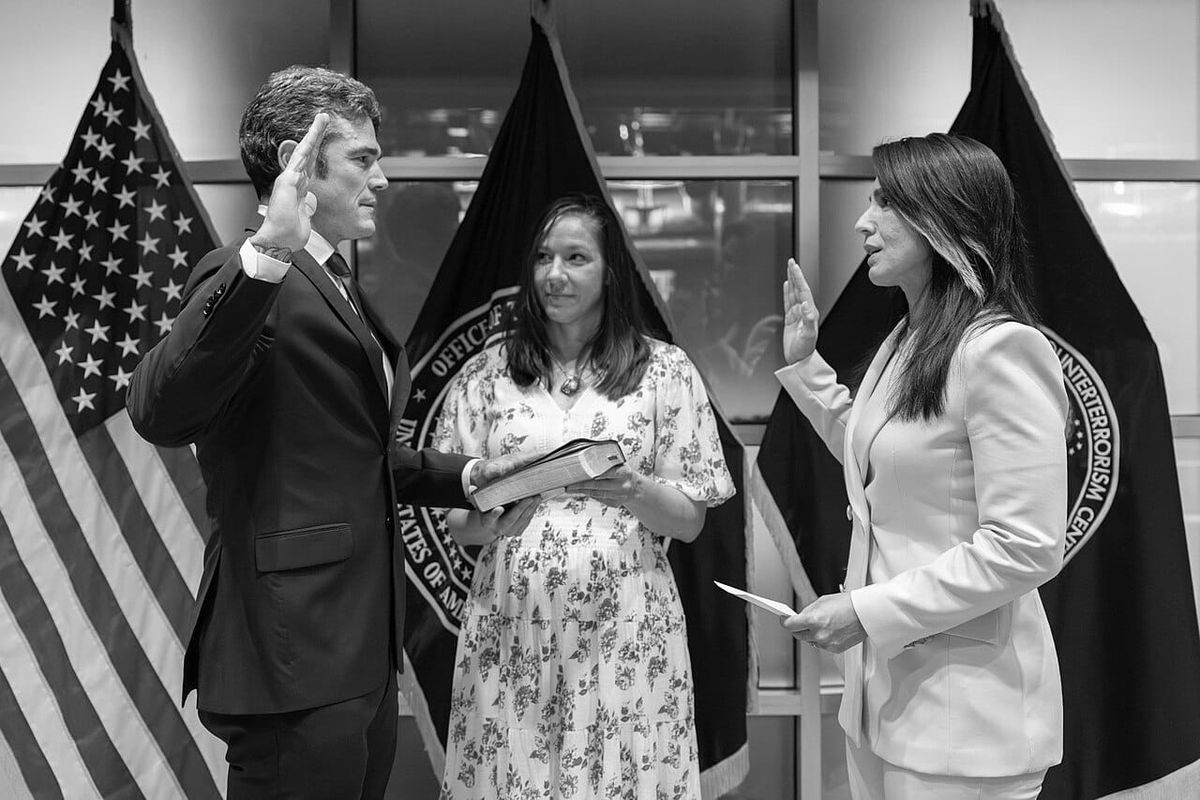 A man in a suit holds up his hand taking oath of office as two officials swear him in.