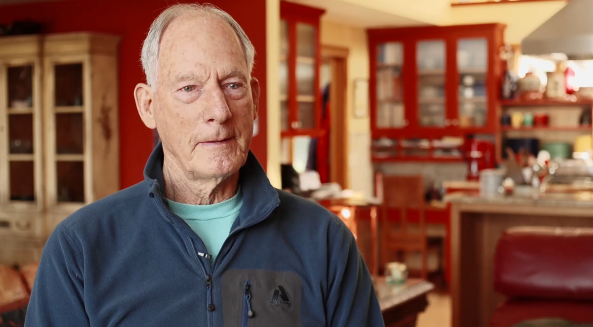 An older man in a fleece and t-shirt stands in front a well-appointed kitchen
