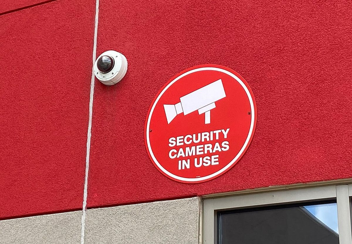 A dome-style secruity camera above a store door with the sign that reads: security cameras in use