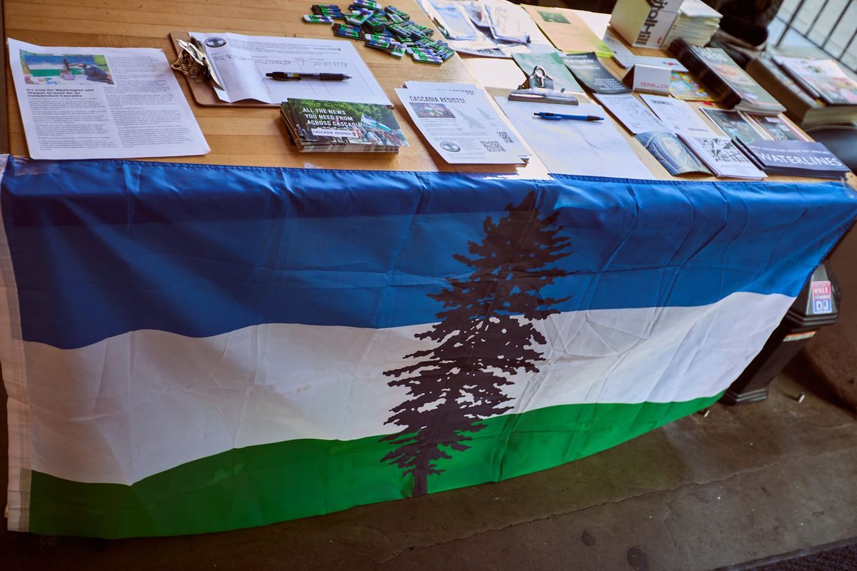 A blue white and green Cascadia Doug flag on a table with brochures, pamplets, and books.