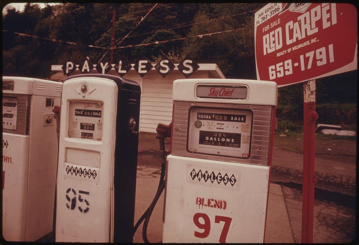 Three old style gas pups and a for sale sign.